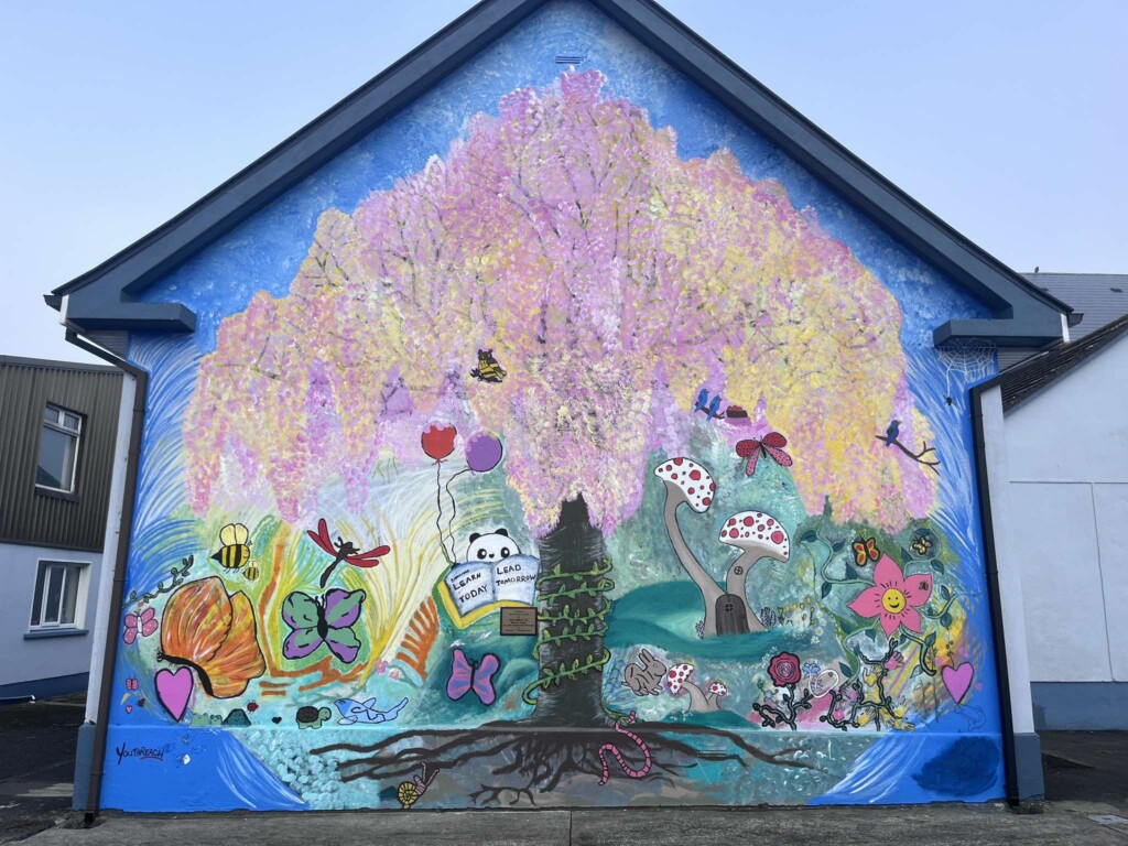 Colourful mural on the side of a building depicting insects, a cherry blossom tree, flowers and nature