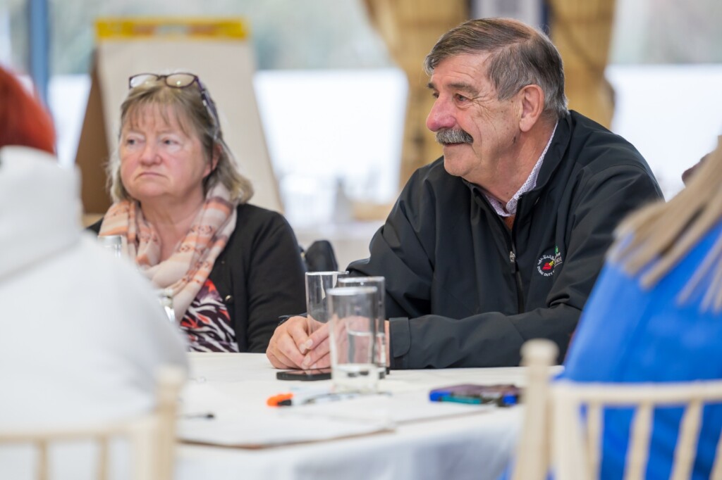 Two older adults sit at a table during a group discussion.