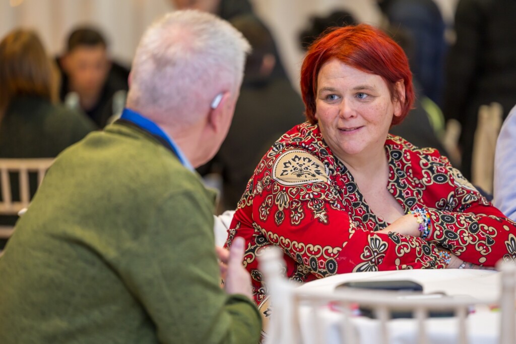 Two older adults sit at a table during a group discussion.