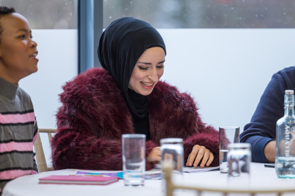 A woman wearing a black headscarf smiling while looking down at papers.
